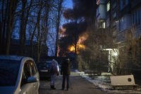 Residents watch at a burning infrastructure project hit during a massive Russian drone night strike in Kyiv