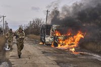Ukrainian soldiers pass by a burning bus.