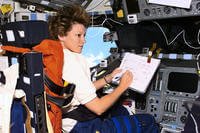 Commander Eileen Collins consults a checklist while seated in the flight deck commander's seat.