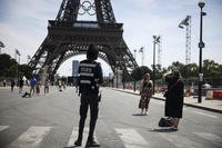 A security officer watches people take photographs in front of the Eiffel Tower.