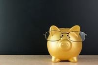 A golden piggy bank wearing glasses appears against a black background