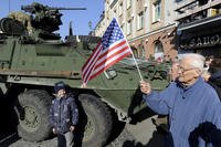 Man holding a US flag walks past a US Army Stryker
