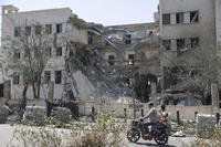 People pass in front of the Syrian Defense Ministry building which on Wednesday was heavily damaged by Israeli airstrikes in Damascus, Syria