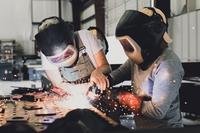 A teacher and student in protective hoods work in a machine shop.
