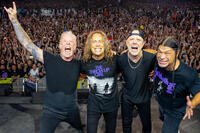 Metallica members pose onstage in front of a massive cheering crowd during a live concert. Photo credit: Brett Murray