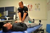A chiropractor presses on a soldier who is lying on his back on a table.