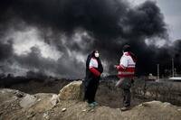 Two women stand together as smoke rises from an oil storage facility in the sky in Iran.