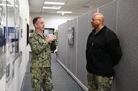 Two Navy officers talk in a hallway.