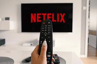 Woman holding remote in front of a television as Netflix boots up. Photo Credit: Creative Commons