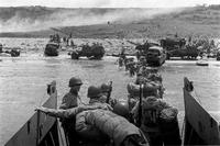 U.S. troops wade ashore from a LCVP landing craft, off &quot;Omaha&quot; Beach, 6 June 1944. Note DUKWs and half-tracks at the water line, lines of men headed inland, and M1903 and M1 rifles carried by some of the troops leaving the landing craft. 6 June 1944