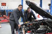Two mechanics standing over an engine.