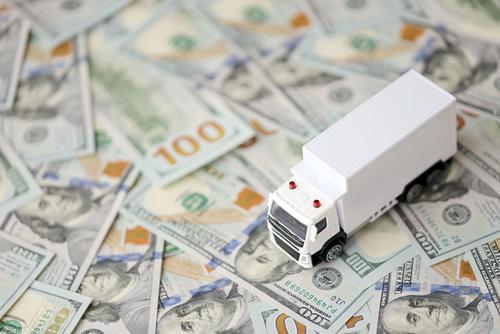 A toy moving truck is on top of scattered U.S. $100 bills.