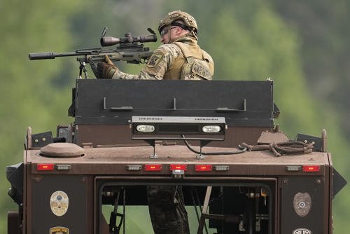A law enforcement officer trains his rifle towards a house as the officers search for shooting suspect Vance Boelter
