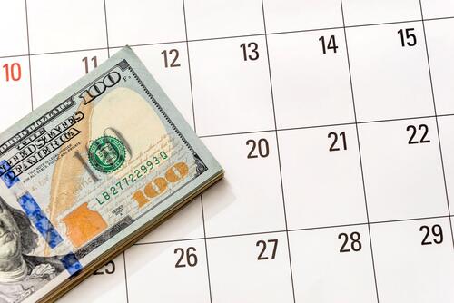 A stack of U.S. $100 bills on top of a generic calendar page.